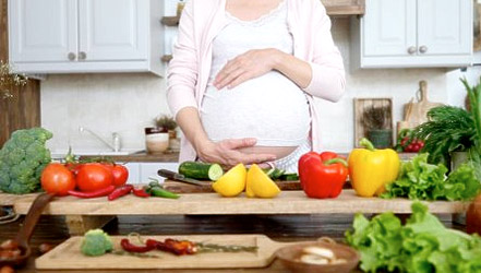 Ein schwangeres Mädchen macht einen Salat aus Paprika und anderem Gemüse